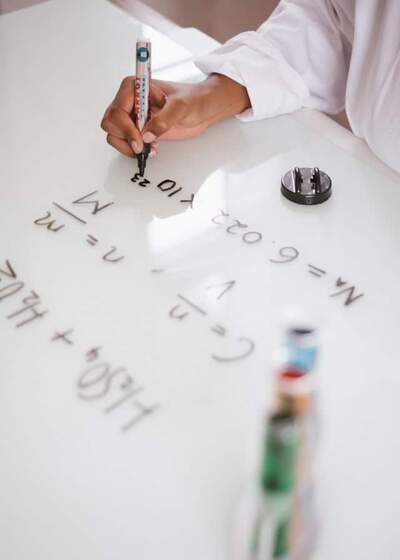 Photograph of scientists hands working on a chemical formula on a whiteboard