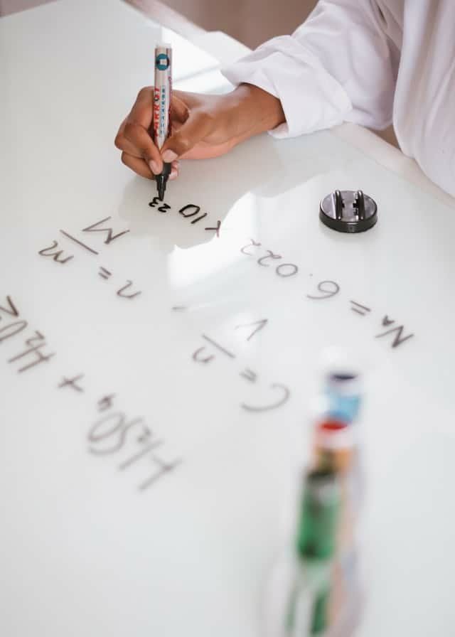 Photograph of scientists hands working on a chemical formula on a whiteboard