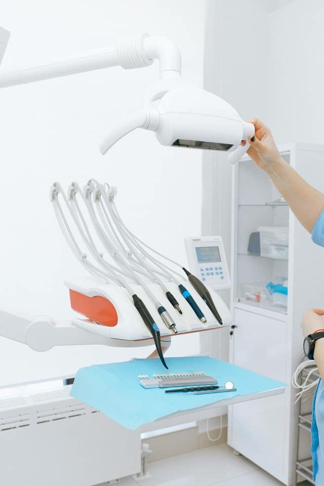 Photograph of dentist adjusting light over an examination chair with dental tools laid out